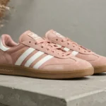 Paire de sneakers Adidas Samba Rose coloris rose poudré sur étagère en béton avec herbes de pampa séchées, finitions cuir blanc et semelle gomme