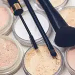 three makeup brushes on top of compact powders