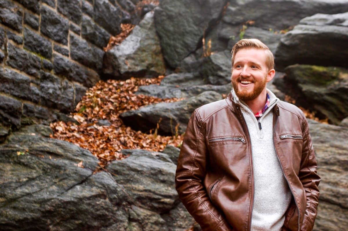 man in brown leather jacket standing near gray rocks during daytime