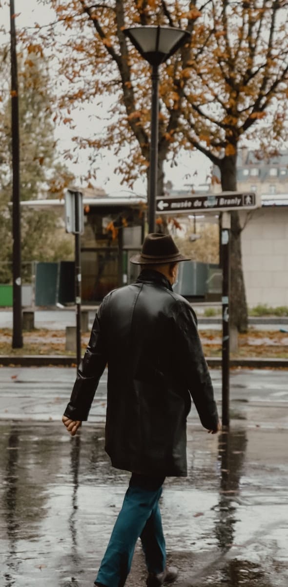 man in black leather jacket and black hat walking on sidewalk during daytime