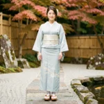 Femme japonaise en yukata bleu pâle avec sandales geta en bois sur un chemin de jardin zen traditionnel