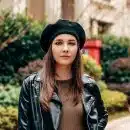 woman in black leather jacket and brown hat standing near green plants during daytime