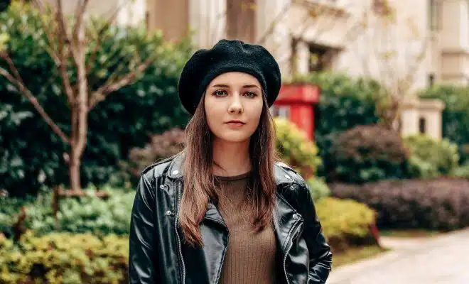 woman in black leather jacket and brown hat standing near green plants during daytime